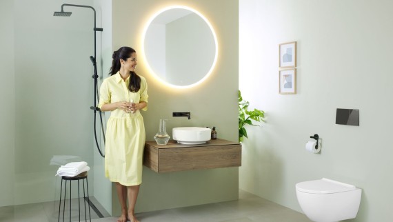 Woman in yellow dress standing in front of mint green bathroom with furniture and bathroom ceramics from Geberit and black taps Woman in yellow dress standing in front of mint green bathroom with furniture and bathroom ceramics from Geberit and black taps